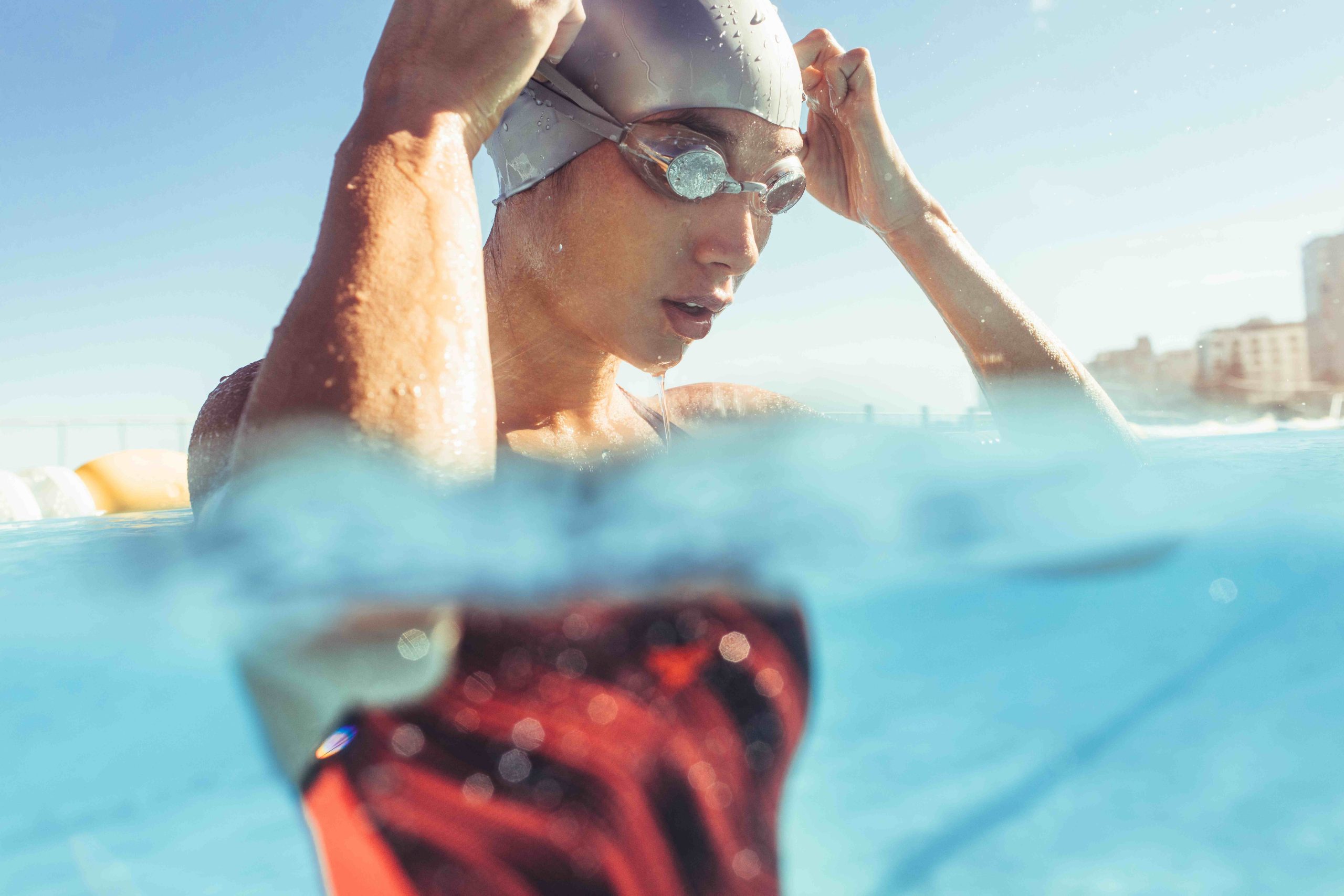 Woman standing in pool wearing swim cap and goggles.