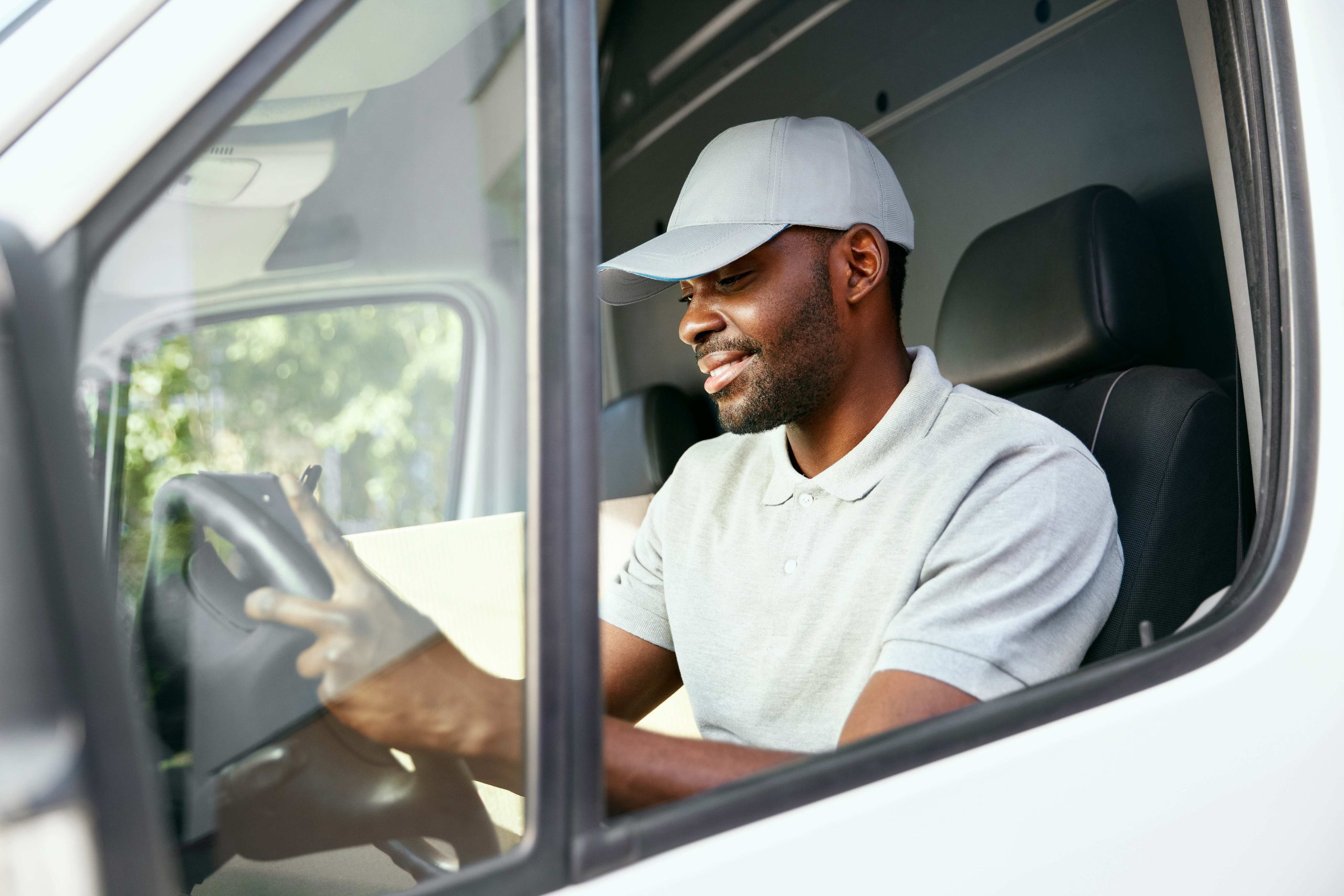 A man in a plain white uniform driving a delivery truck.