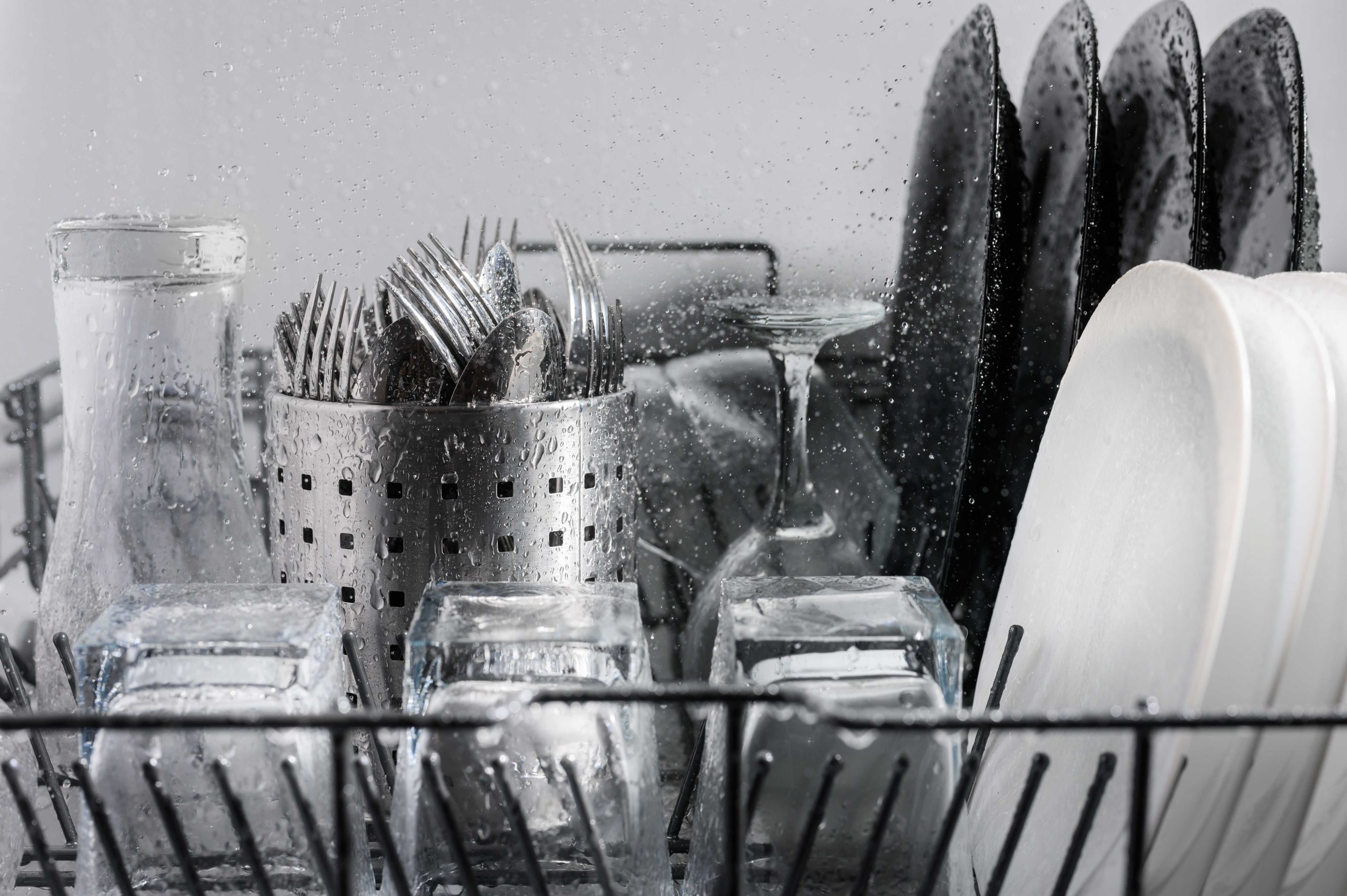 Wet flatware, cups, plates, bowls, dishes in a stainless steel dishwasher.