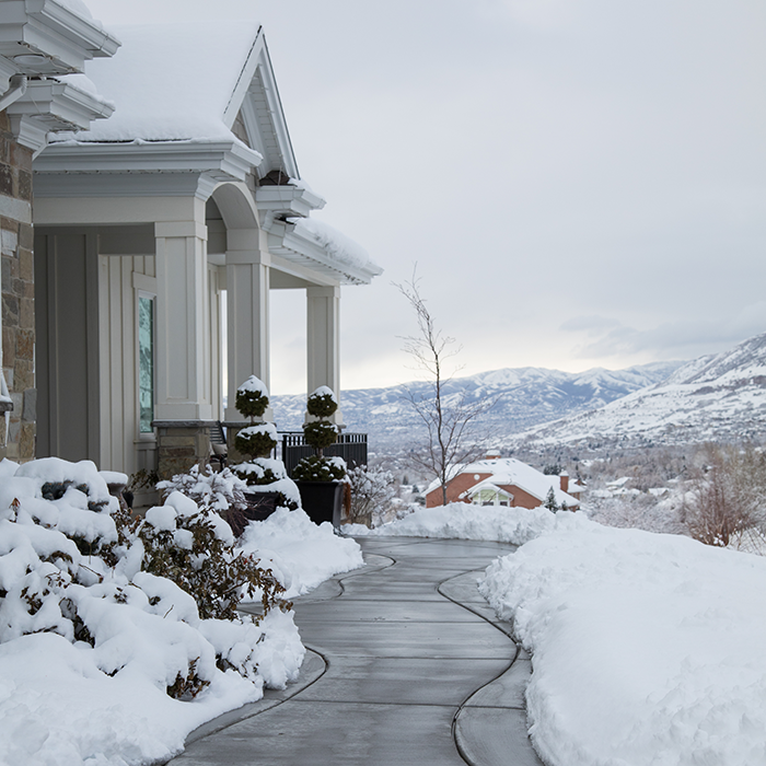 A snow-covered house with a clear walkway surrounded by piles of snow.