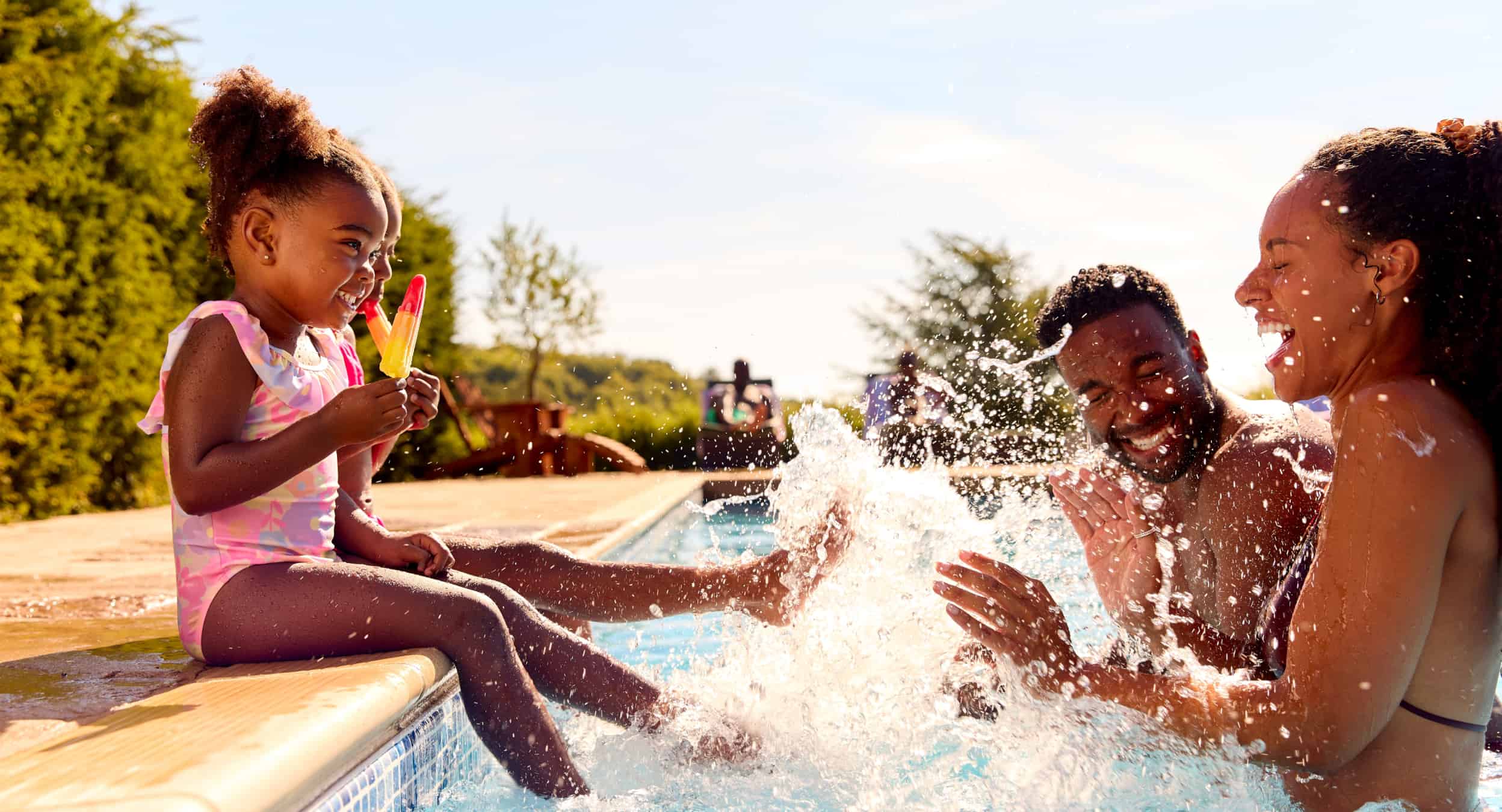 Two adults and two young children splashing around in a pool together.